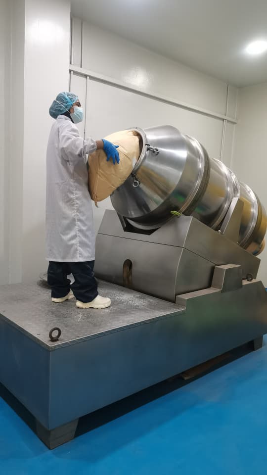 Gowned operator charging a stainless steel double-cone blender with premix powder