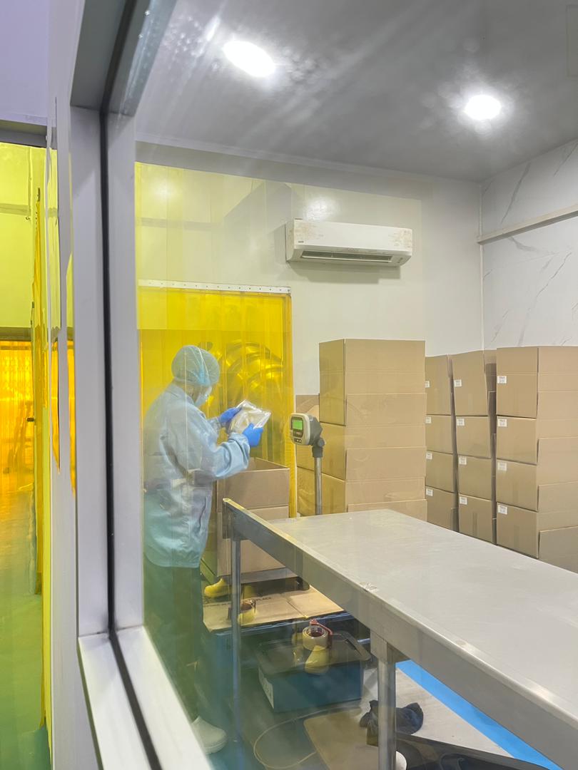 Packing room seen from the corridor, with an operator in gown and hairnet working at the scale