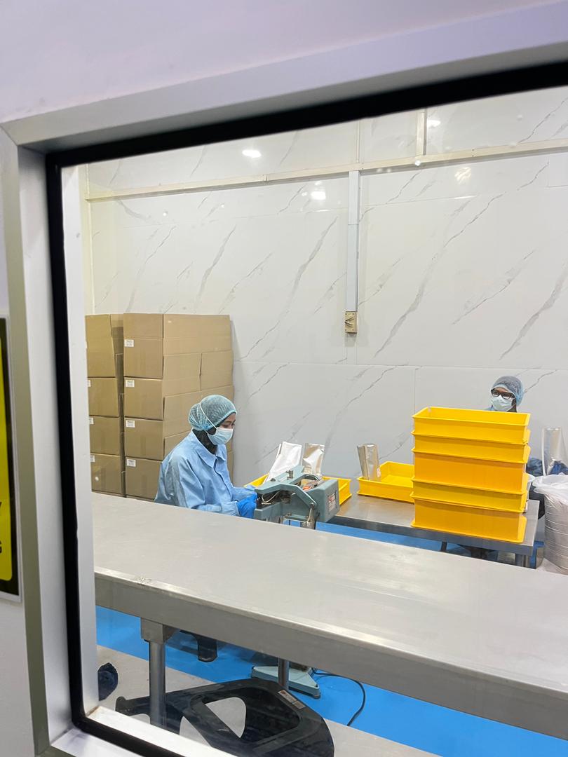 Two gowned operators heat-sealing filled foil bags at a stainless steel bench