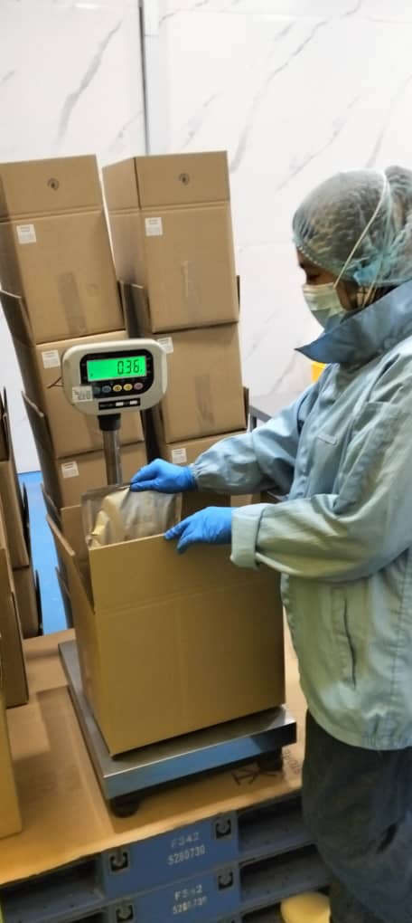 Gowned operator in gloves weighing a sealed foil sachet of premix powder on a platform scale